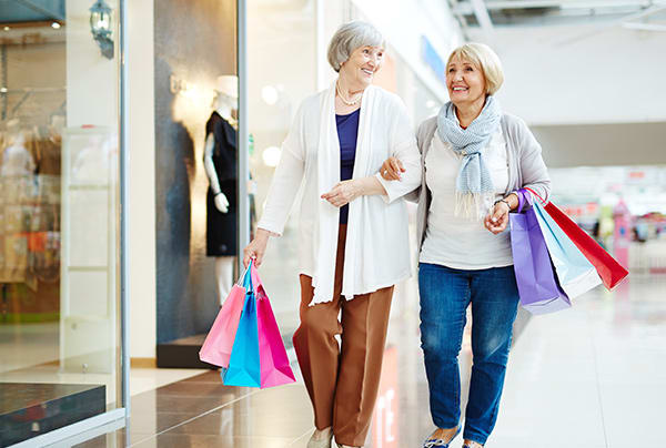 Two senior women walk arm in arm while shopping in a mall